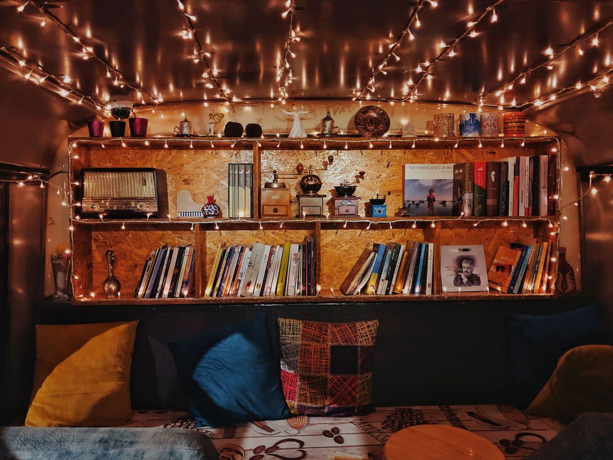 A warm and inviting reading corner with bookshelves, fairy lights, and colorful cushions.