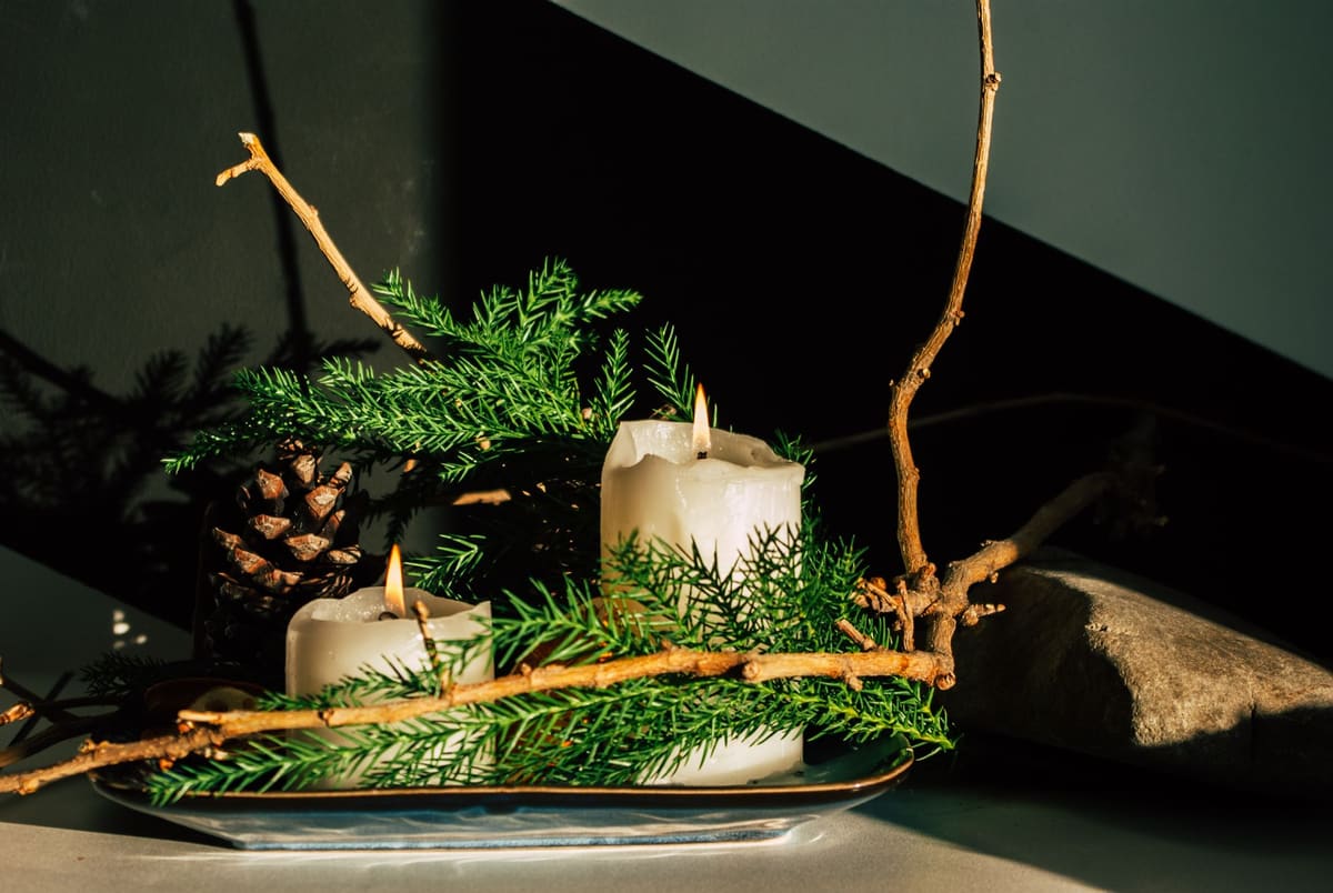 A warm candlelit setup featuring pine branches and pinecones, perfect for holiday decor.
