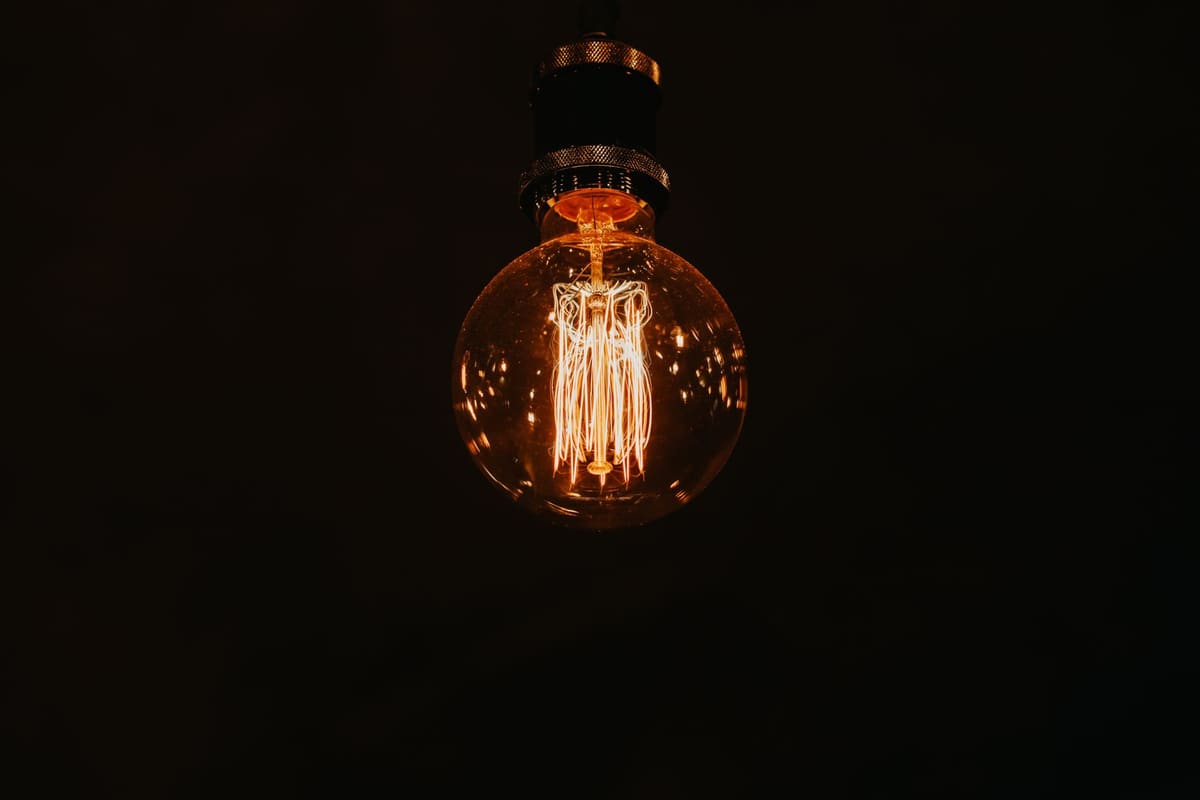 From below of glowing stylish lamp with warm light hanging in dark room