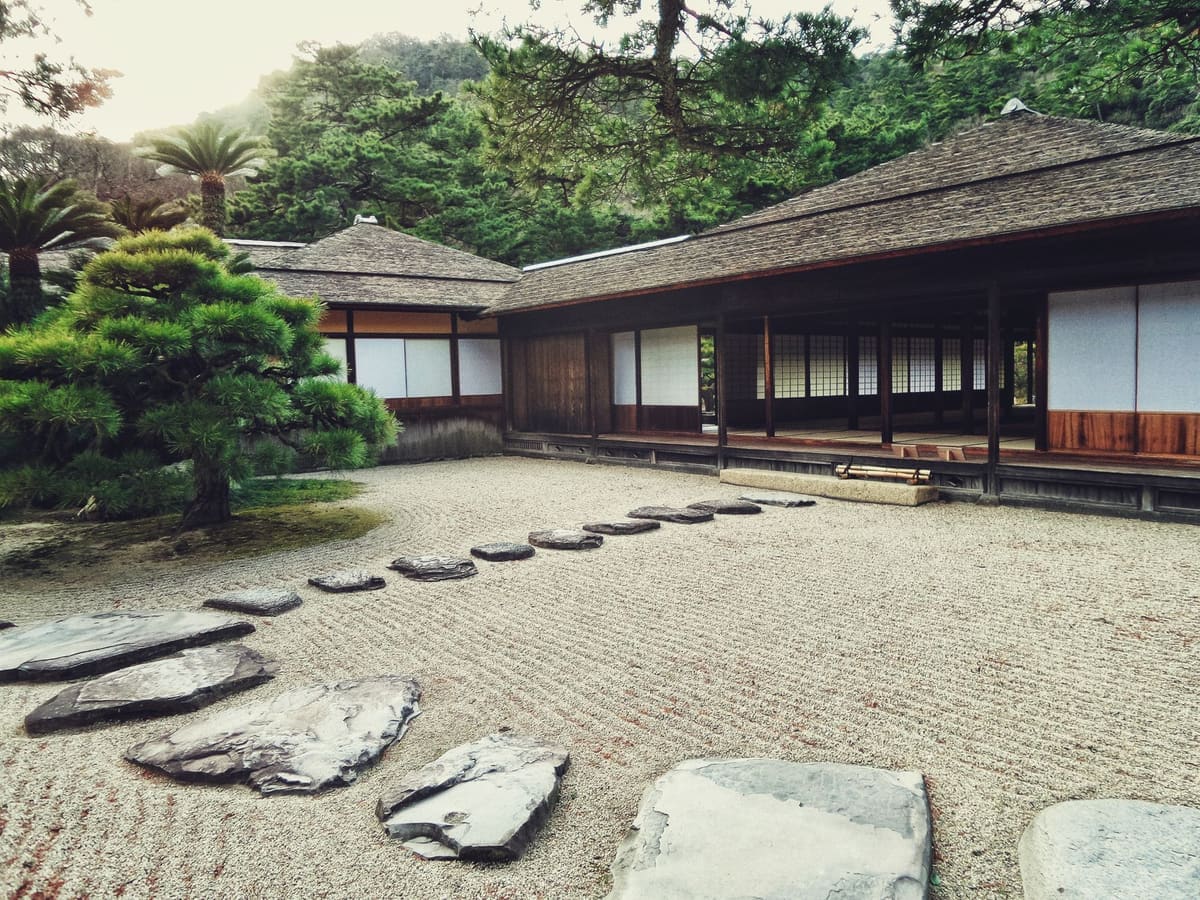 Serene Japanese Zen garden with stone path, lush greenery, and traditional wooden architecture.