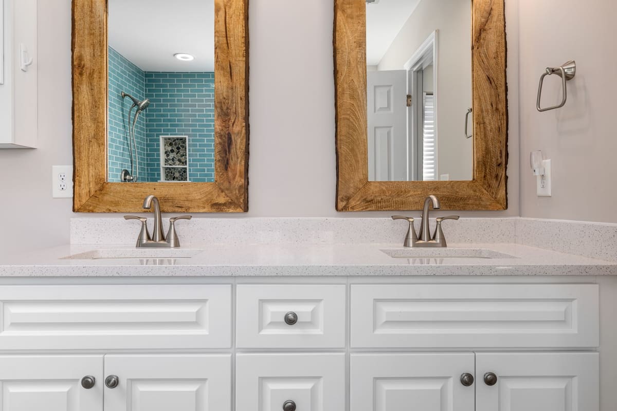 Elegant bathroom featuring double sinks, wooden mirrors, and blue tiled shower.