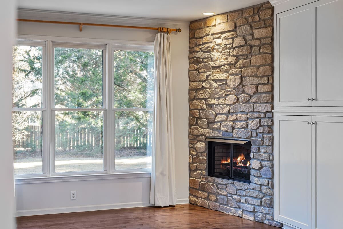 Inviting living room featuring a stone fireplace, large windows, and hardwood floor.