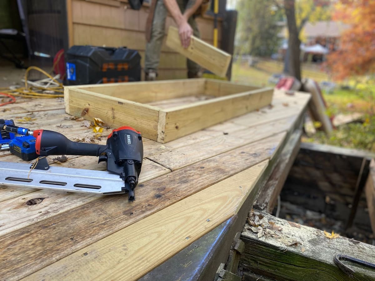Close-up of carpentry work on a deck with a nail gun and wooden frame under construction.