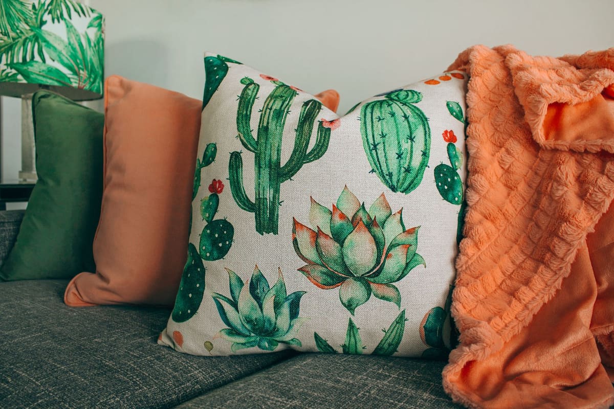 A stylish living room setup with cactus-themed pillow and soft orange blanket.