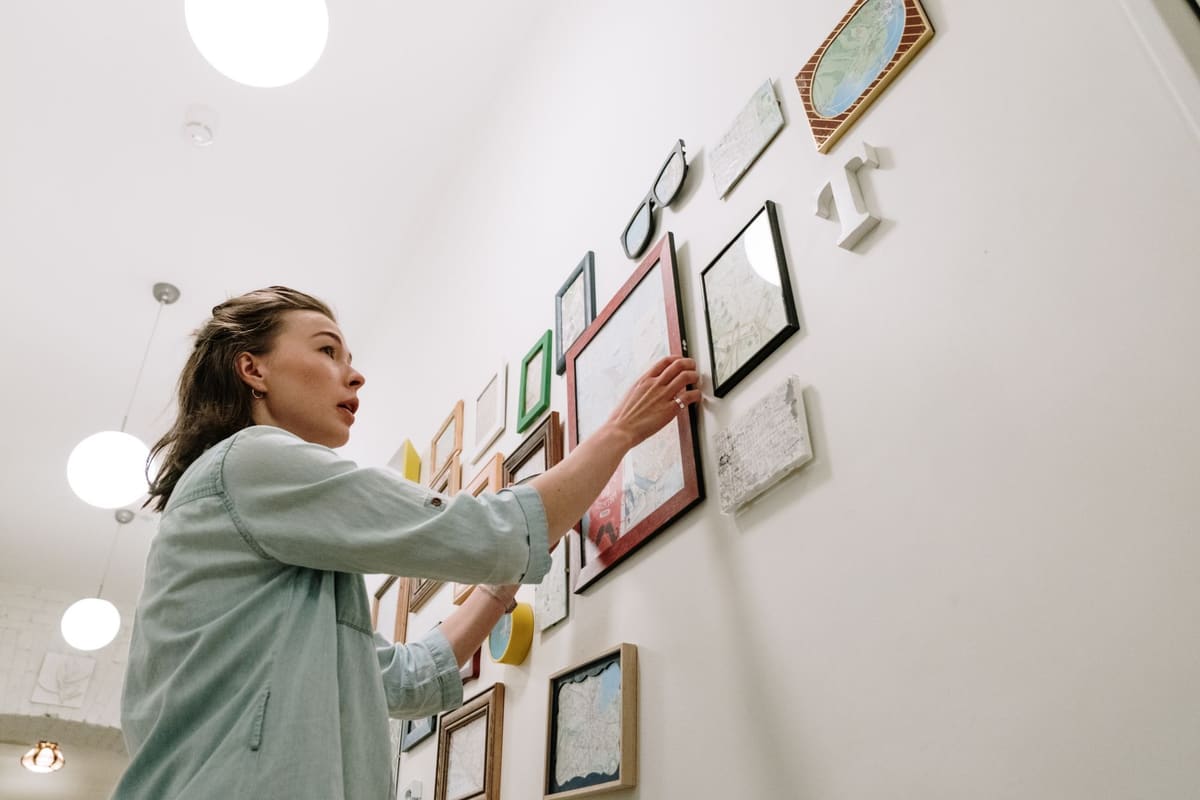 A woman arranging picture frames on a bright indoor wall
