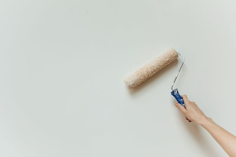 Close-up of a hand painting a wall with a roller brush during renovation.