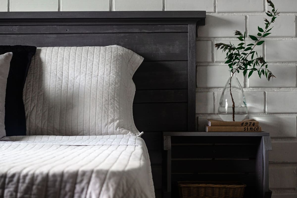 Chic rustic bedroom with cozy bedding, modern nightstand and glass vase.