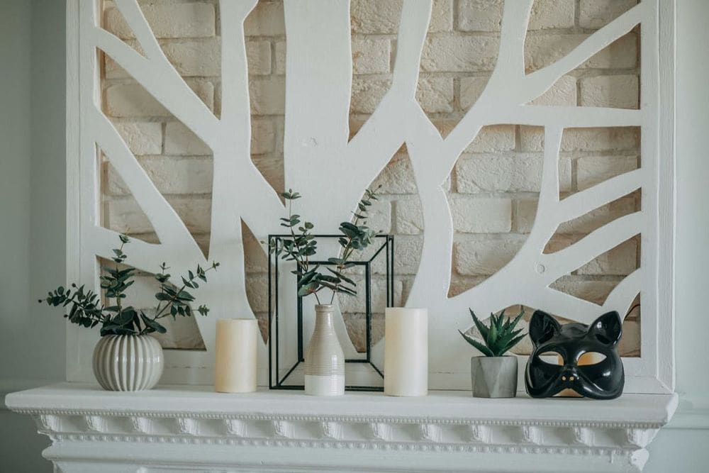 A stylish mantel display featuring candles, vases, plants, and a decorative mask against a modern backdrop.