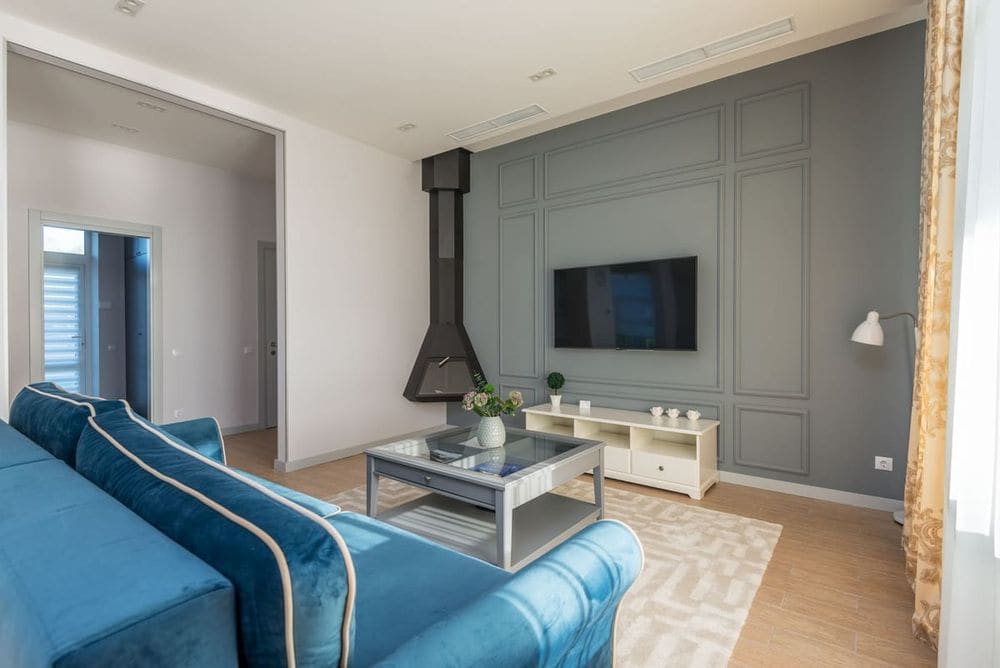 A stylish living room featuring a blue couch, wall-mounted TV, and elegant decor.