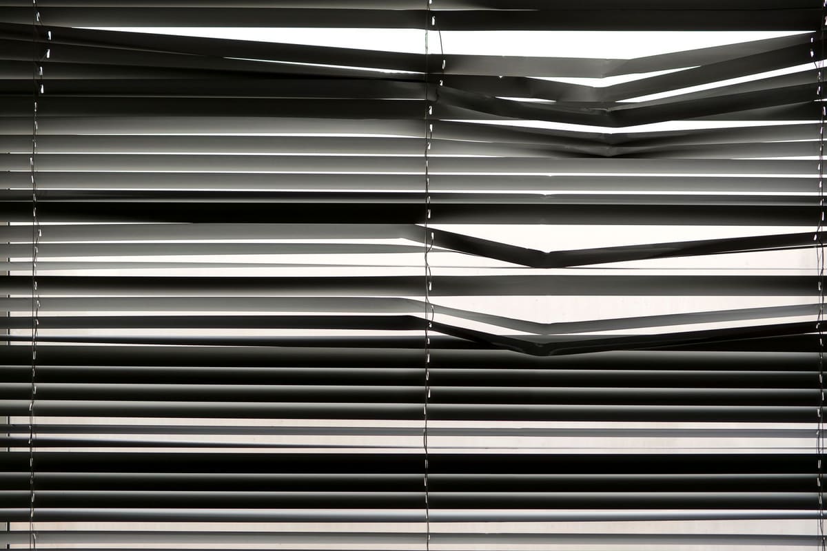 Horizontal venetian blinds creating a shadow pattern indoors with strong sunlight.